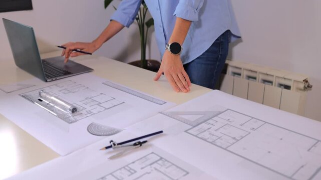 Female architect drawing house blueprints using professional tools and a laptop. Engineer creating building project sketches in her office with technical equipment and a computer