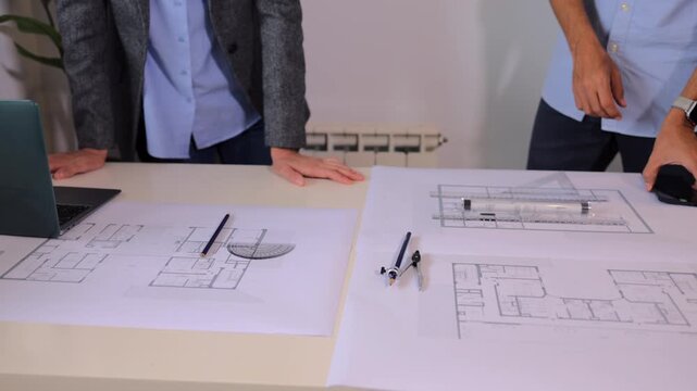 Two architects collaborating on a blueprint, discussing the building construction plan and drawing with professional technical tools on a white office desk