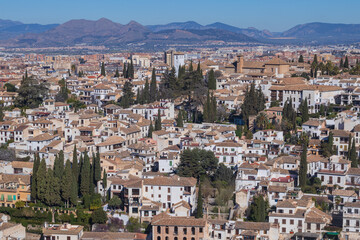 Fototapeta premium Panorámica del histórico barrio del Albaicín con sus casas blancas y tejados tradicionales, visto desde la Alhambra. Al fondo se divisan las montañas bajo un cielo azul en Granada, España.