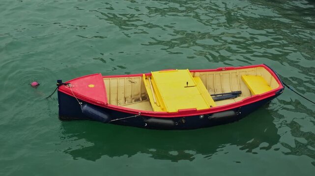Top-down view of a red, yellow, and blue boat swaying on waves near a buoy