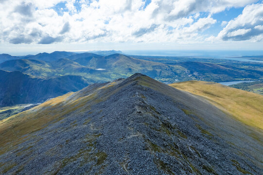 Aerial view of rugged, rocky peaks stretching towards the horizon under a sky dappled with clouds, where shadows dance across the landscape, Caernarfon, Wales, United Kingdom.