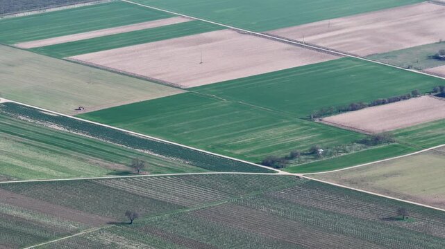 Aerial view of lush green and brown agriculture fields divided by roads, creating a patchwork quilt of textures and tones, Mittelwihr, Grand Est, France.