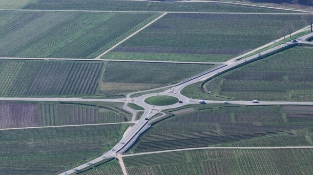 Aerial view of a roundabout amidst vineyards creating a patchwork of greens and browns, roads cutting through, Mittelwihr, Grand Est, France.