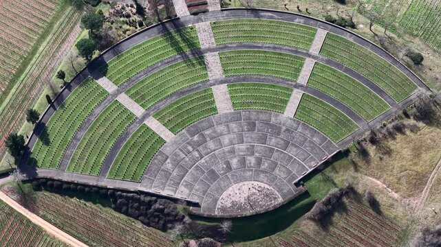 Aerial view of a semi-circular war cemetery with rows of tombstones, surrounded by vineyards, creating a poignant scene, Mittelwihr, Grand Est, France.