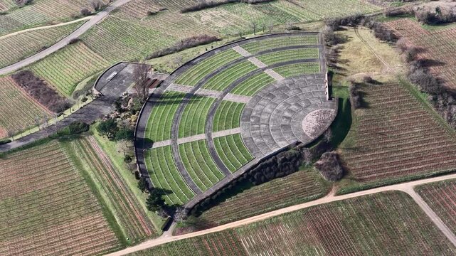 Aerial view of the stark Memorial, a semi-circular monument amidst vineyards, creating a striking contrast of grey stone and cultivated land, Mittelwihr, Grand Est, France.