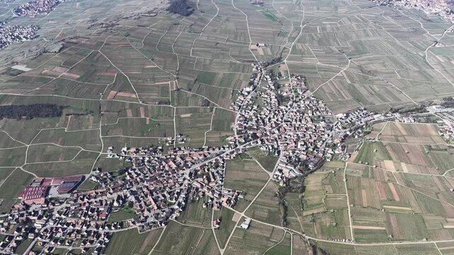 Aerial view of Mittelwihr village, surrounded by patchwork fields in varying shades of green and brown, highlighting the landscape's textures, Mittelwihr, Grand Est, France.