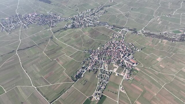Aerial view of Mittelwihr village surrounded by geometric vineyards, showcasing a blend of rural architecture and agricultural landscape, Mittelwihr, Grand Est, France.