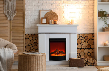 Naklejka premium Interior of living room with shelving unit, folding screen, wicker coffee table and firewood near fireplace