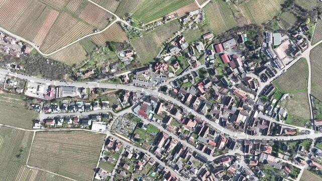Aerial view of rooftops interspersed with roads and verdant fields, casting contrasting shadows in the landscape, Mittelwihr, Grand Est, France.