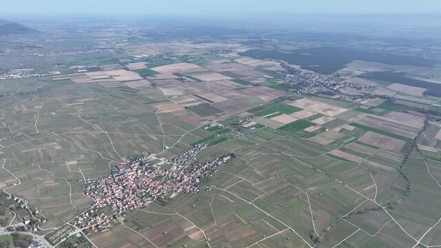 Aerial view of the village amidst patchwork fields, a symphony of greens and browns, in Mittelwihr, Grand Est, France.