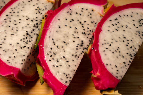 rhythmic arrangement of three fresh dragon fruit (pitaya) wedges on a light wooden cutting board, showcasing the vibrant magenta skin and seed-speckled white pulp.