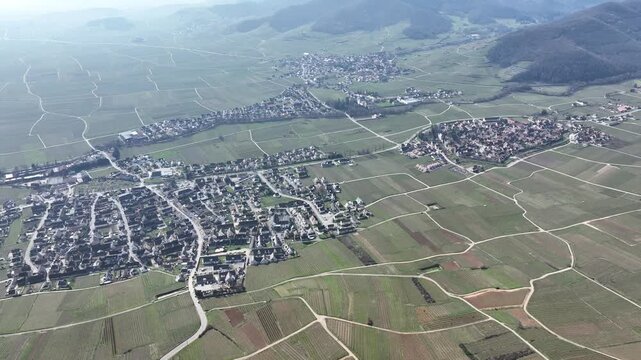Aerial view of the village surrounded by patchwork fields, where the lush greenery meets the quaint rooftops, creating a serene landscape, Mittelwihr, Grand Est, France.
