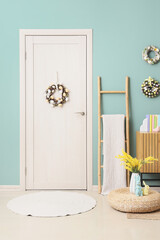 Interior of festive room with commode, ladder, ottoman, flowers and Easter wreaths hanging on blue...