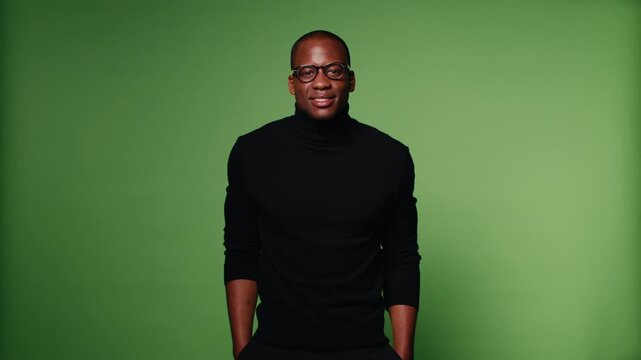 Confident man in a black turtleneck and glasses poses against a green screen