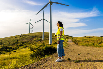 Woman engineer wearing high visibility vest standing near wind turbines