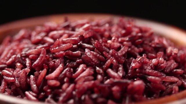 Cooked riceberry rice in a wooden bowl rotating slowly on black background. Close-up view