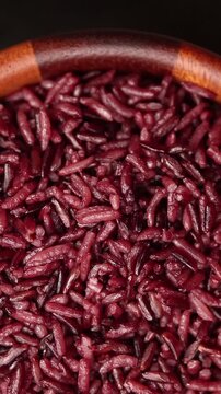 Cooked riceberry rice in a wooden bowl rotating slowly on black background. Top view shot