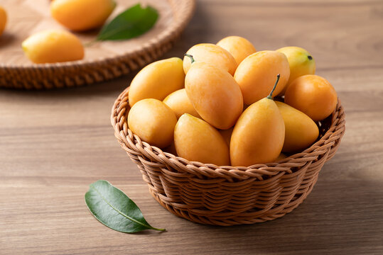 Fresh Marian plum (Mayongchid) in a wicker basket on wooden background, Thai tropical fruit in summer season
