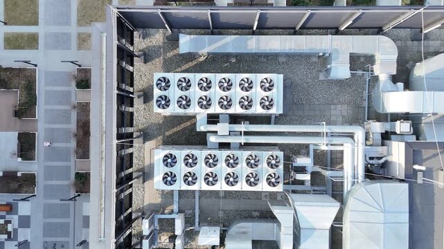 Ventilation system on the roof of a modern building featuring multiple air conditioning units, ducts, and a gravel surface, with surrounding urban landscape visible in the background
