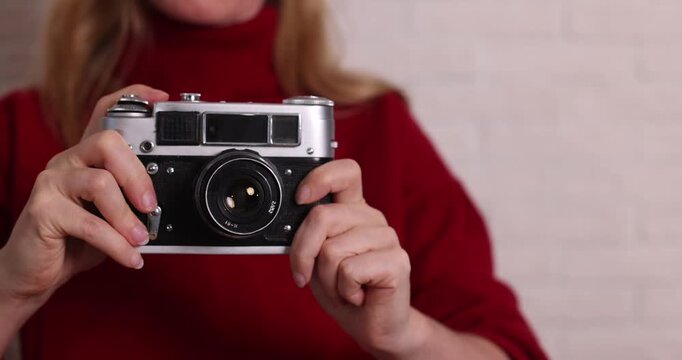 Woman in red sweater holding a retro camera against white brick wall, photographer, vintage style, nostalgia, photography hobby, studio