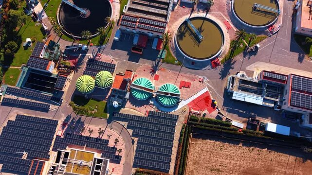 Circular clarifiers and solar panel arrays. High angle vertical shot showing circular sedimentation tanks, sludge digesters, and photovoltaic panels at a facility.