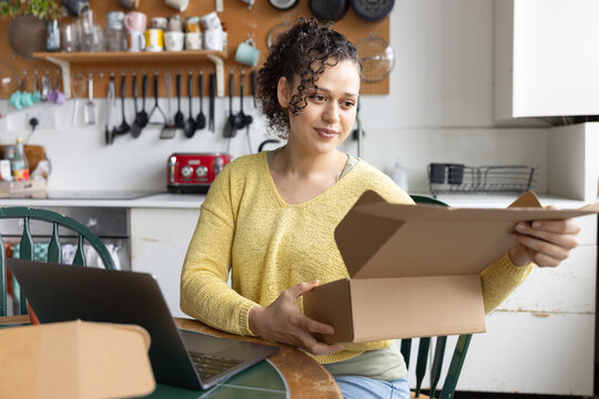 Happy young female entrepreneur looking at order details from e-commerce site and preparing parcels to ship