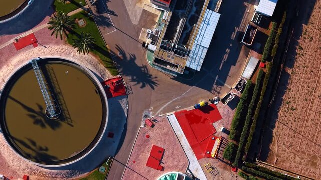Circular secondary clarifier and facility grounds aerial. Close up high angle view of a rotating clarifier bridge and the paved area of a treatment plant.