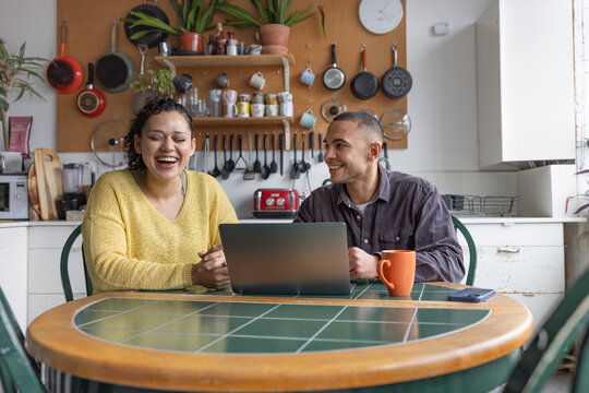 College students laughing together while using laptop in a kitchen