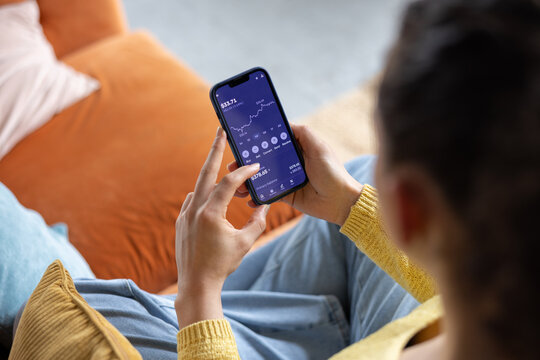 Over the shoulder view of young woman with friend checking financial data with mobile banking app on a smartphone
