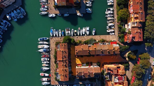 Aerial view of marina docks and residential roofs. Straight down view of terracotta tiled roofs, palm trees, and yachts moored in a narrow canal in Spain.