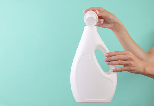 Woman's hand holds mockup of white bottle of liquid laundry detergent or soap on a mint-colored background