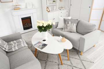 Naklejka premium Interior of light living room with sofas, tables and white roses in vase