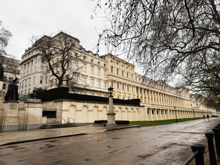 Naklejka premium Elegant neoclassical Carlton House Terrace building along a tree-lined street in London, UK, during cloudy day with promenade