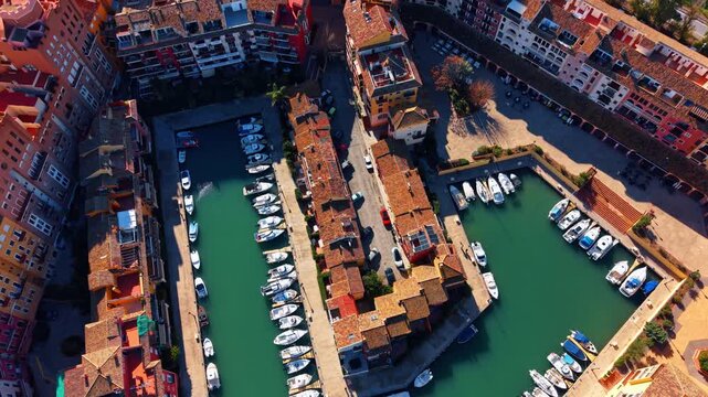 High angle view of residential marina with moored yachts. Aerial shot of Mediterranean town houses surrounding a basin filled with private boats and parked cars.