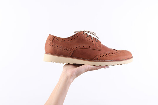 Hand holding leather brown brogue boot on white background