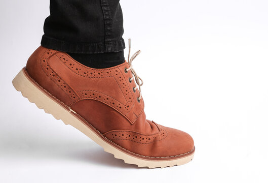 Man's leg in slim jeans and brown leather brogue shoe on a white background. Men's style