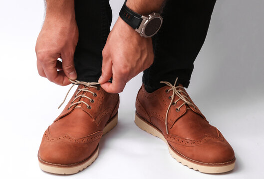 Man is tying the shoelaces of brogues on a white background