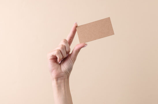 Hand holding Cardboard brown bisiness card on a beige background