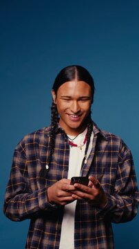 Young man smiles while looking at his phone against a blue backdrop