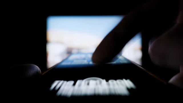 Finger rapidly scrolls through an endless social media feed on a smartphone screen. Shallow depth of field and motion blur emphasize speed and information overload in a dark room.