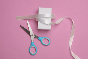 White box with satin ribbon and scissors on a pink background. Holiday packaging