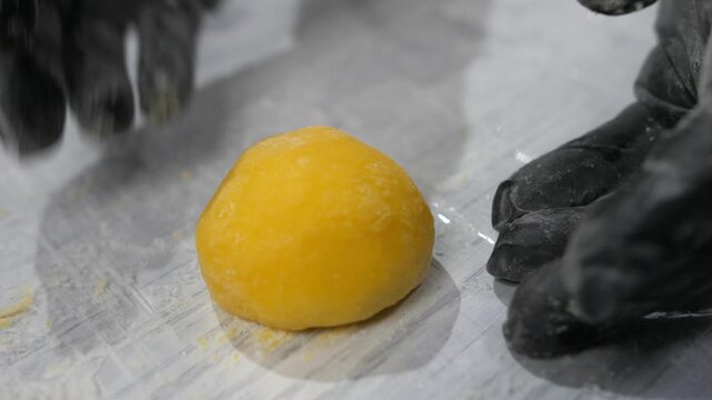 Baker hands shape form and add powdered sugar to mango mochi cake in bakery closeup. Professional confectioner decorates Japanese dessert with tropical fruits in kitchen. Healthy sweets