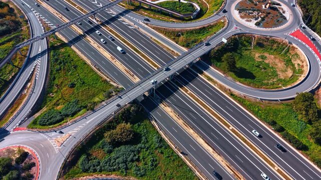 Aerial view of highway roundabout and overpass junction. High angle shot of complex road infrastructure with roundabout, bridge and surrounding greenery.