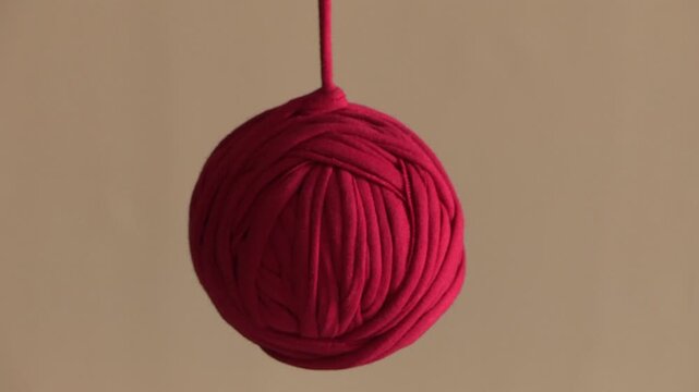 A red thread coiled into a ball shape, hanging down and sliding.