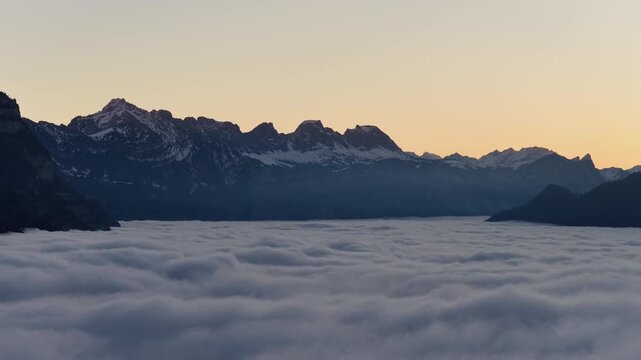 Aerial sunrise view above cloud inversion over Walensee lake with dramatic Alpine mountains in Switzerland.