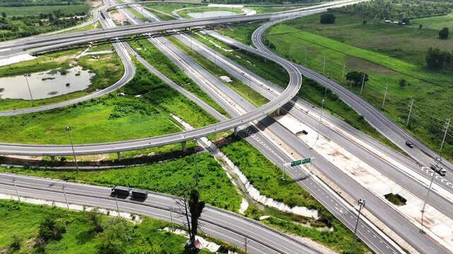 Aerial view of modern highway interchange with multilayer roads and curved ramps surrounded by green farmland, showcasing transportation infrastructure, urban development, and road network planning.