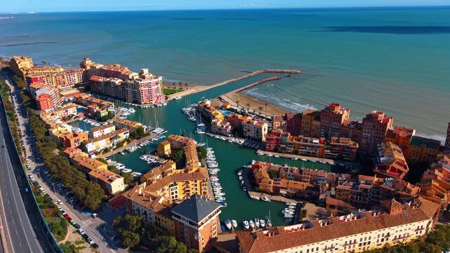 Port Saplaya beach and marina. High angle shot of colorful buildings along the Mediterranean coast with breakwater and blue sea.