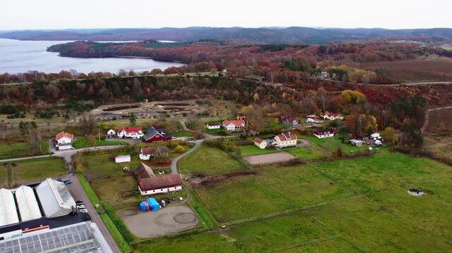 Aerial drone view of farms and villas at Fjaras Bracka in Sweden surrounded by autumn forest, open fields, countryside roads, and lake landscape in rural Scandinavian environment