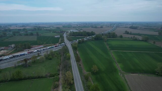 Line of trucks and vehicles halted along a highway interchange cutting through agricultural countryside with traffic heading northbound