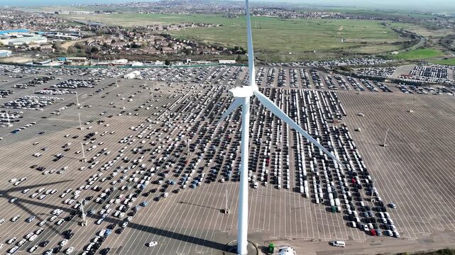 Aerial view Wind Turbine with new car imports parked in background Sheppey UK